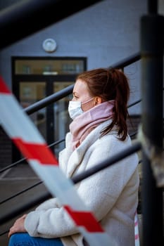 Photo of a girl in a mask. Sitting on the street with danger warning tapes. isolated Covid-19 pandemic.