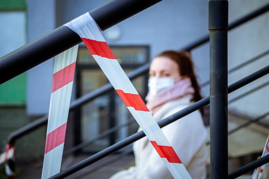 Photo of a girl in a mask. Sitting on the street with danger warning tapes. isolated Covid-19 pandemic.