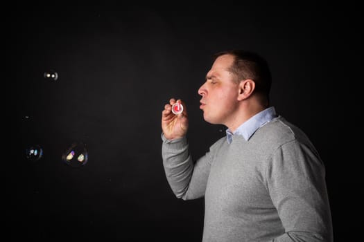 handsome man in a suit is blowing soap bubbles. isolated on a black background