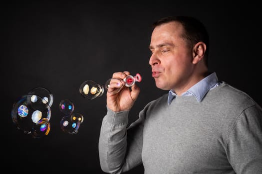 handsome man in a suit is blowing soap bubbles. isolated on a black background