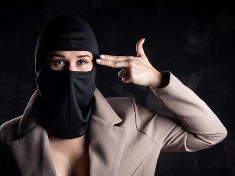 Portrait of a girl in a black balaclava and beige coat. Shot in the studio on a dark background.