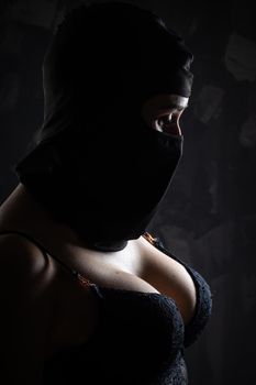 Portrait of a girl in a black balaclava and a black bra. Shot in the studio on a dark background.