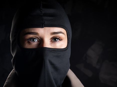 Portrait of a girl in a black balaclava and beige coat. Shot in the studio on a dark background.