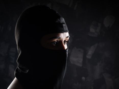 Portrait of a girl in a black balaclava and a black bra. Shot in the studio on a dark background.