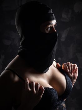 Portrait of a girl in a black balaclava and a black bra. Shot in the studio on a dark background.