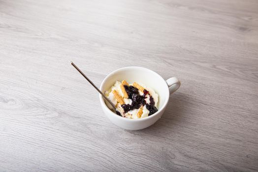 ice cream with blackberry jam in a white cup on a wooden light background