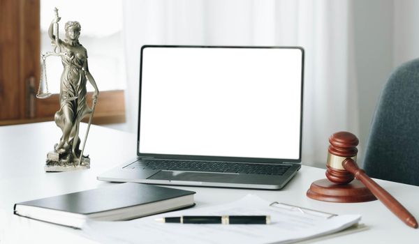 Workspace of lawyer with laptop blank white screen and law wooden gavel, and brass scale of judge. courtroom legal concept..