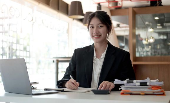 Beautiful smiling Asian woman working at the office, looking at the camera..