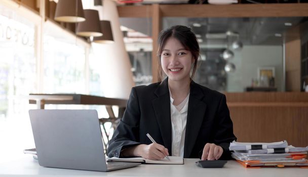 Beautiful smiling Asian woman working at the office, looking at the camera..