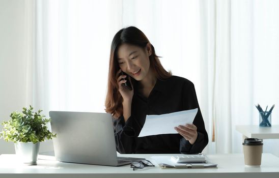 Beautiful young Asian businesswoman charming smiling and talking on the mobile phone in the office..