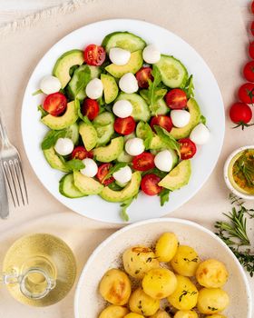 Fresh salad with tomatoes cucumbers, arugula, mozzarella and avocado. Oil with spices, baked potatoes, top view, vertical