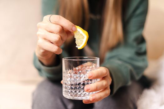 Young woman holding lemon slice and glass of water, closeup