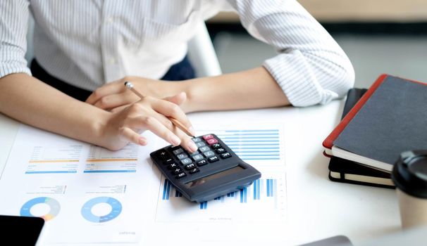 Asian accountant working and analyzing financial reports project accounting with chart graph and calculator in modern office, finance and business concept..