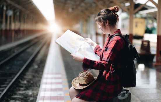 Pretty Young traveler woman looking on maps planning trip at public train station. Summer and travel lifestyle concept.