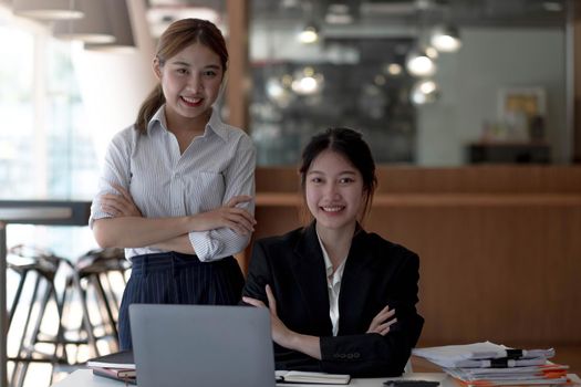Two attractive beautiful Asian businesswomen sit and talk and look at the camera..