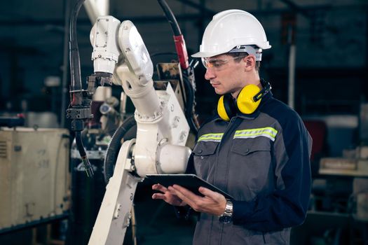 Young factory worker working with adept robotic arm in a workshop . Industry robot programming software for automated manufacturing technology .
