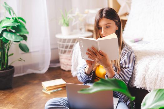 Distance learning online education and work. Business woman writes in notebook, sitting on the floor. Happy and smiling girl with laptop at home office. Using computer and online shops.