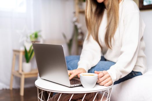 Distance learning online education and work. Business woman with coffee cup typing at laptop, sitting on the couch near the plants. Freelance girl woking from home office. Using computer and shopping.