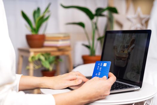 Freelance woman with credit card typing at laptop and online shopping, near the plants. Happy girl woking from home office. Distance learning online education and work.