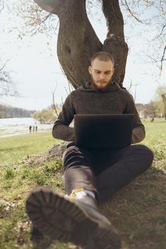 Young man using and typing laptop computer in summer grass.