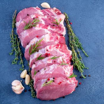 Pork steak, raw carbonate fillet on dark background, meat with rosemary, garlic seasonings, top view.