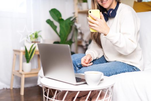 Freelance woman with headphones and laptop, taking selfie at mobile phone. Sitting on the couch, online shopping. Happy girl woking from home office. Distance learning online education and work.