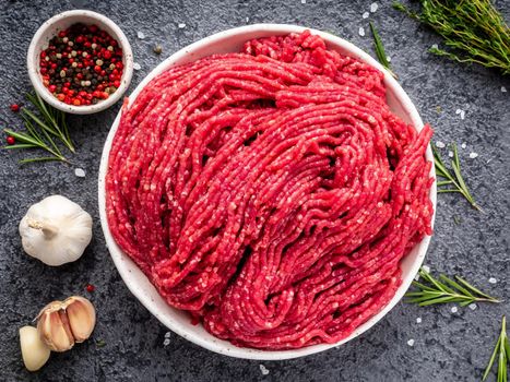 Mince beef, ground meat with ingredients for cooking on dark gray background, top view, close up.