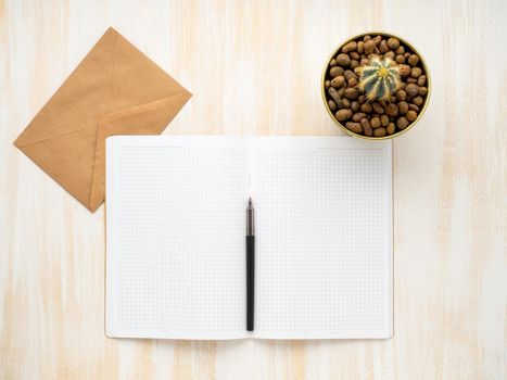 white open notepad, kraft envelope and cactus in pot lying on a beige wooden desk, flat lay, copyspace