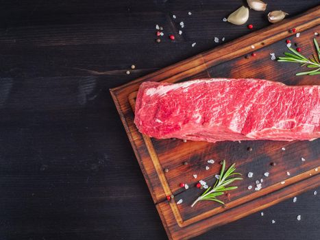 Whole piece of raw meat. Fresh big beef striploin with spices on chopping board on dark background, top view, copy space.