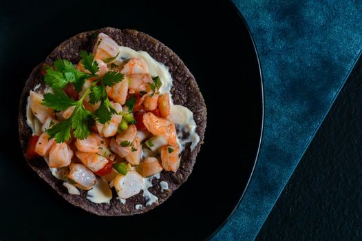 Red shrimp ceviche served with blue corn tostadas. Mexican food. Low key lighting on black and blue background