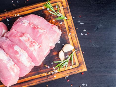 Pork steak, raw carbonate fillet on dark background, meat with rosemary, seasonings, top view.