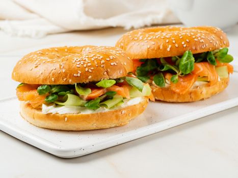 Two sandwiches with salmon, cream cheese, cucumber slices on white marble table