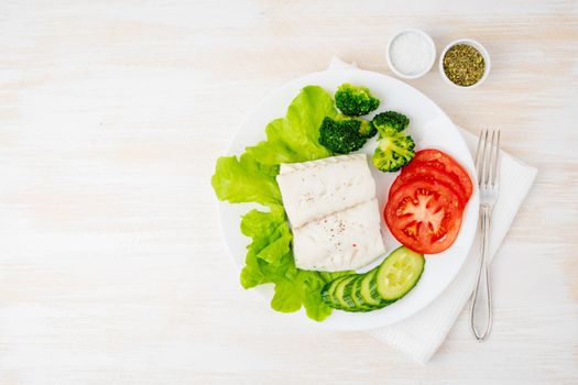 Steamed cod fish. Paleo, keto, fodmap healthy diet with vegetables on white plate on white table, top view, copy space