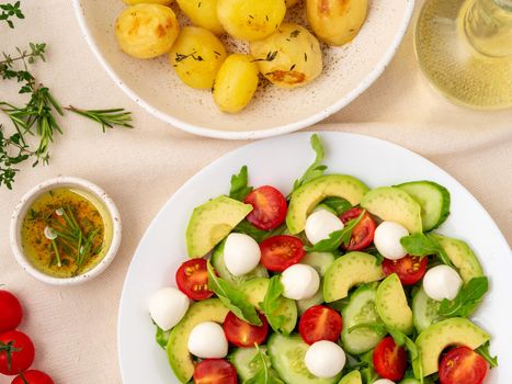 Fresh salad. Tomatoes, cucumbers, arugula, mozzarella, avocado. Fragrant oil with a rosemary thyme and baked potato, top view
