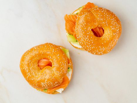 Two sandwiches with salmon, cream cheese, cucumber slices on white marble table