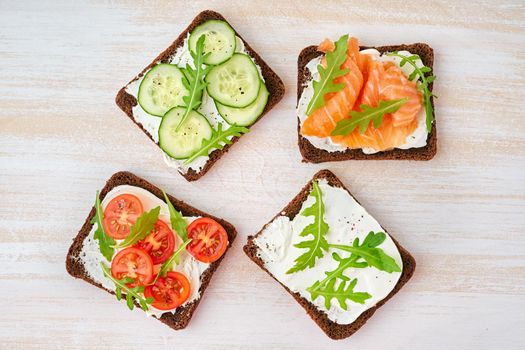 Smorrebrod - traditional Danish sandwiches. Black rye bread with salmon, cream cheese, cucumber, tomatoes on wooden background