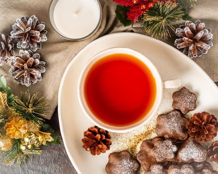 Christmas or new year card. Winter holiday composition, top view, flat lay, brown background. Tea, cookies, fir cones, candles, gift