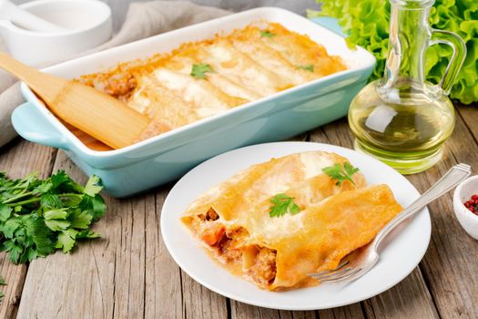 Cannelloni with filling of ground beef, tomatoes, baked with bechamel tomato sauce, side view, old dark wooden background