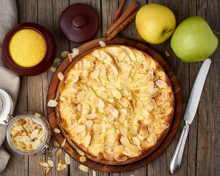 Cheesecake, apple pie, curd dessert with polenta, apples, almond flakes and cinnamon on dark wooden kitchen table, top view