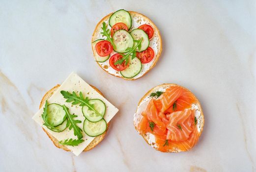 three delicious open sandwiches with salmon, tomatoes, cucumber and cheese on light marble table