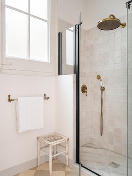 Vintage beige color bathroom with shower zone, window, towel and wooden stool.