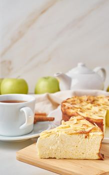 Cheesecake, apple pie, curd dessert with polenta, apples, almond flakes and cinnamon on white marble kitchen table, top view, copy space, vertical