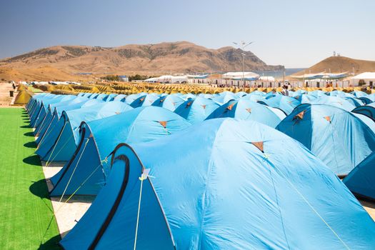 camping with a large number of tourist tents in an improvised festival town on the coast of the warm sea. In the distance you can see showers and toilets for tourists