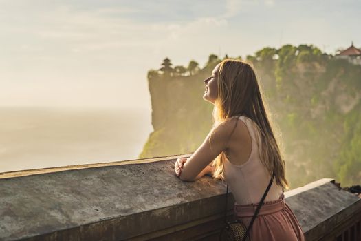 Young woman traveler in Pura Luhur Uluwatu temple, Bali, Indonesia. Amazing landscape - cliff with blue sky and sea.