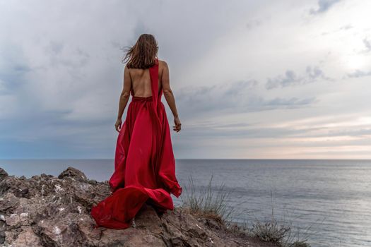 A woman in a red dress stands above a stormy sky, her dress fluttering, the fabric flying in the wind