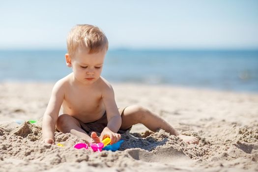 European two year old toddler boy playing with beach toys on beach.