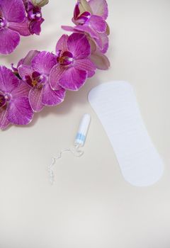 Hygiene supplies during your period, a tampon or pad is placed with a purple orchid flower