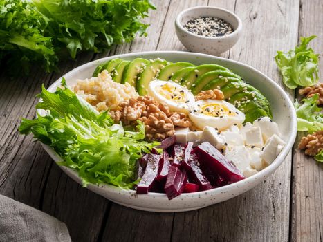 Buddha bowl, balanced food, vegetarian menu. Old wooden dark table, side view. Eggs, avocado, salad lettuce, bulgur, beetroot, tofu