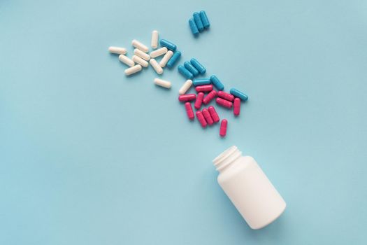 Various multicolored pills flying from an open plastic bottle isolated on a blue background