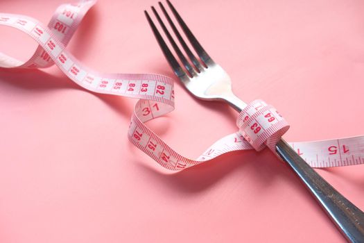 fork with measurement tape on pink background .